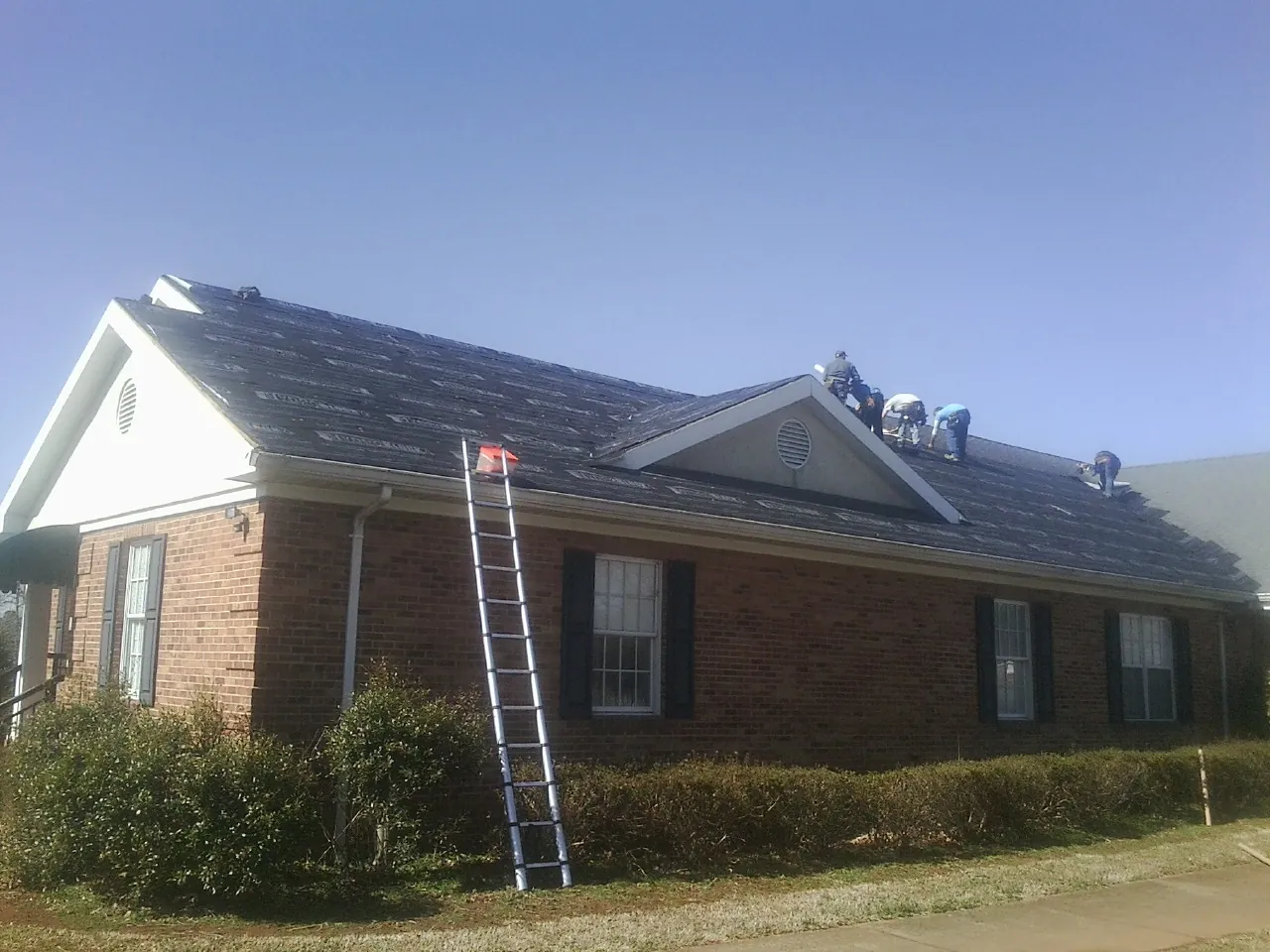 Crew tearing shingles off a brick ranch roof with a ladder set — Emergency Roof Repair work by our crew in Lyons